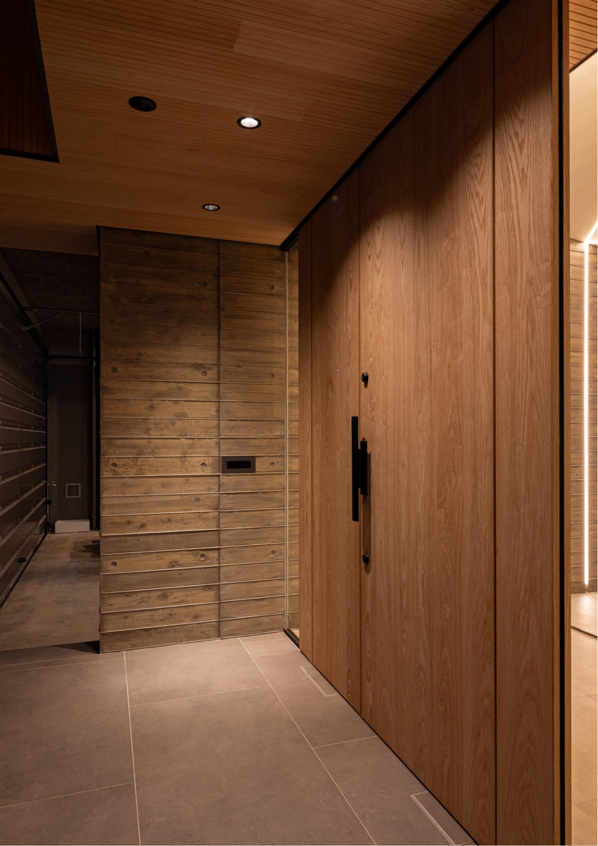 木目調の天井と扉、打ちっぱなし風のコンクリート壁が調和した高級感のある玄関スペース