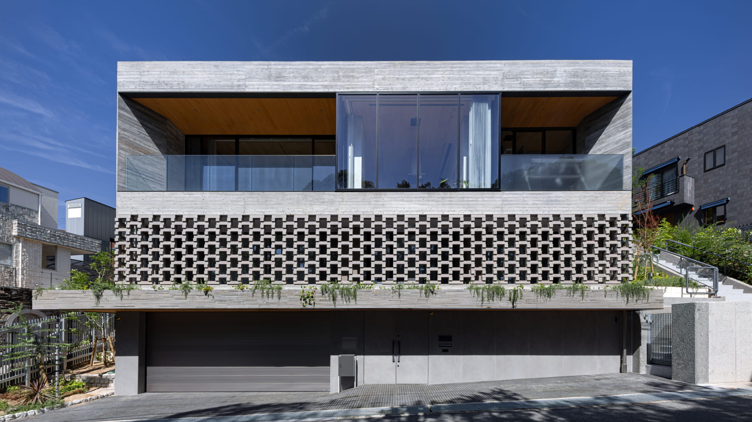 正面から撮影された現代的な住宅で、中央に大きなガラス窓と左右にバルコニーを備えるデザイン