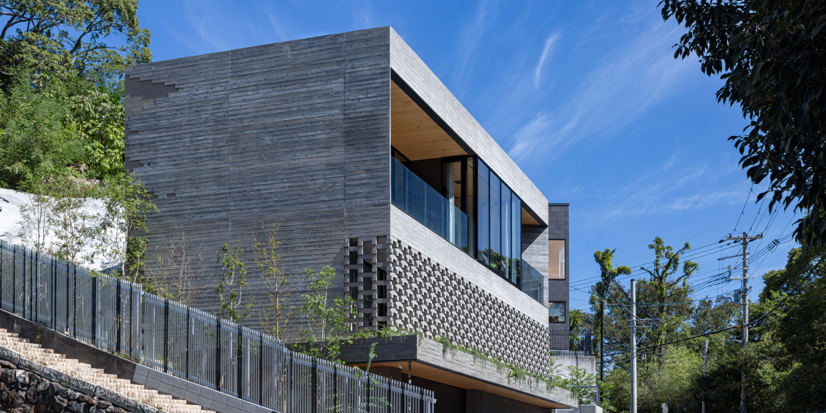 坂道沿いに建てられたコンクリート打ち放しの現代的な住宅を斜めから撮影した外観