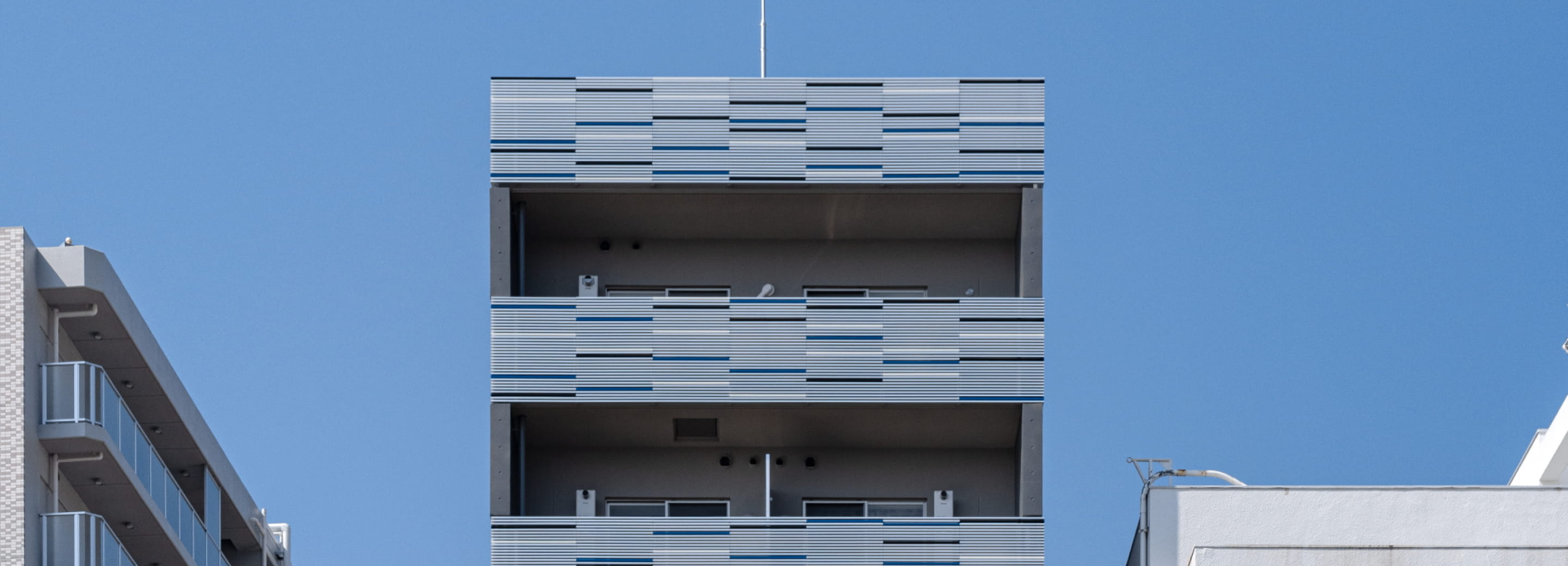 白と青のラインが入ったバルコニーを備える集合住宅の一部を下から見上げた写真