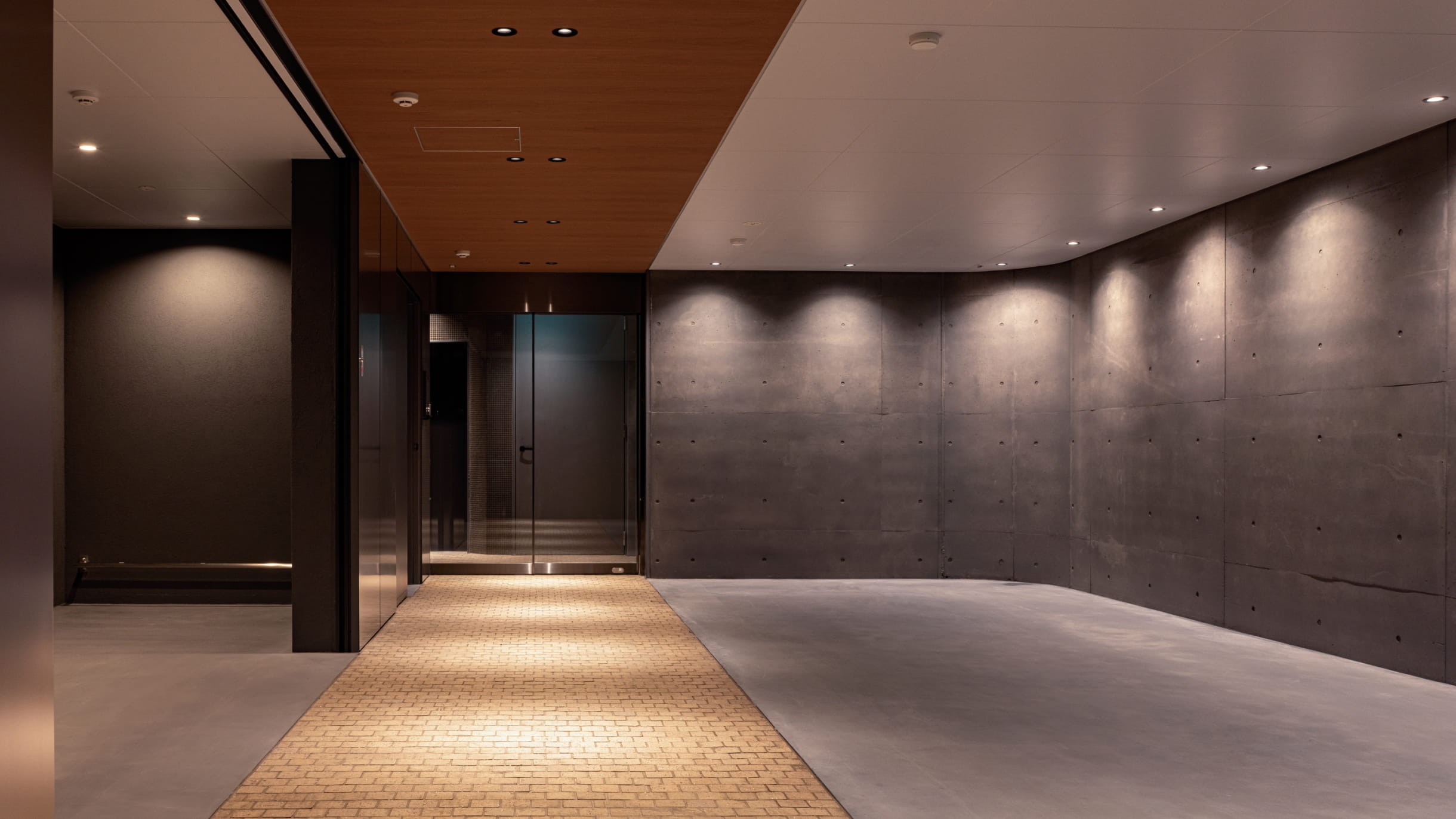 間接照明が照らすマンションのエントランスホール。コンクリート壁と木目天井が特徴