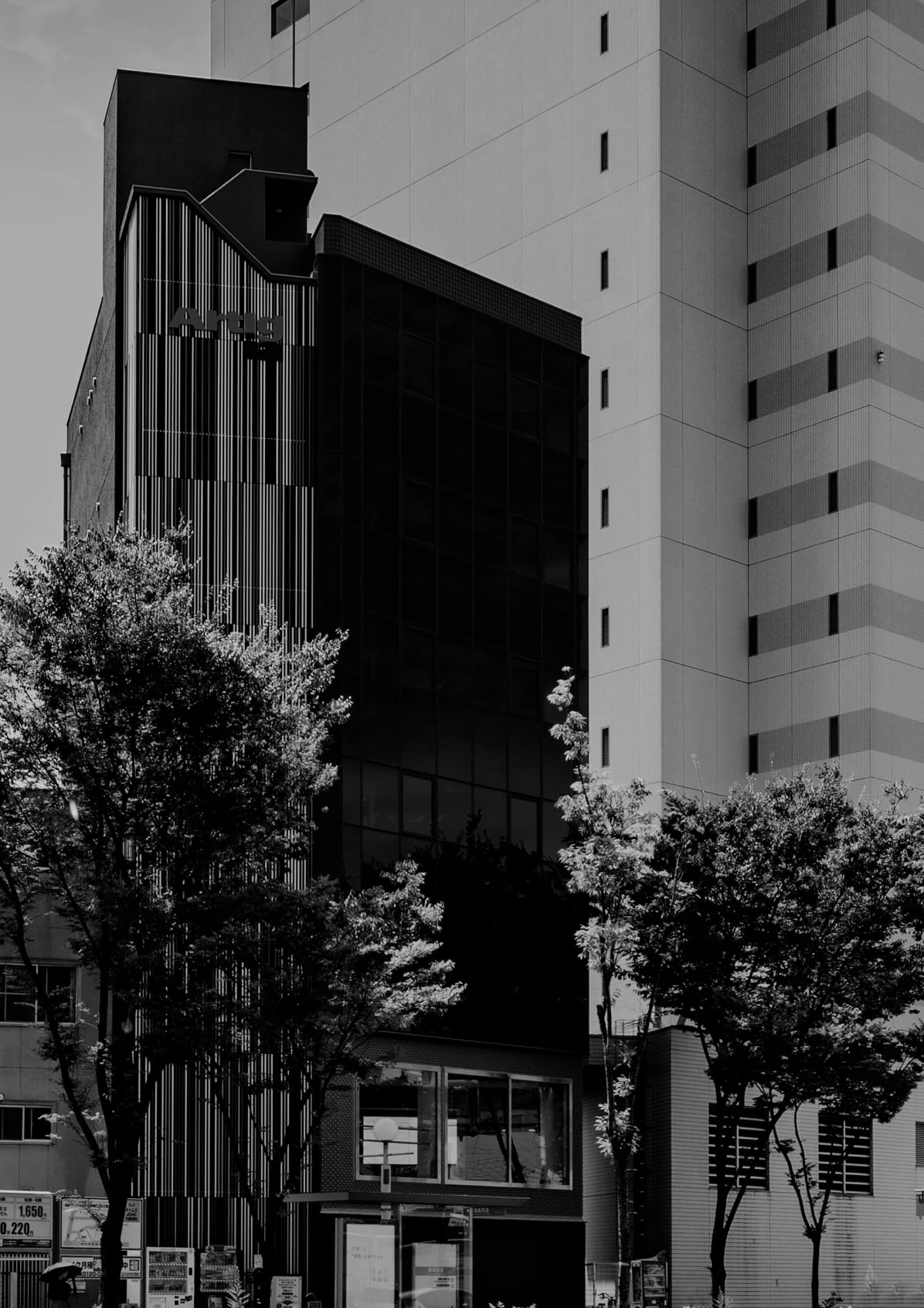 ガラス張りの外観と縦のラインが印象的な、都市部に建つ中層オフィスビルのモノクロ写真