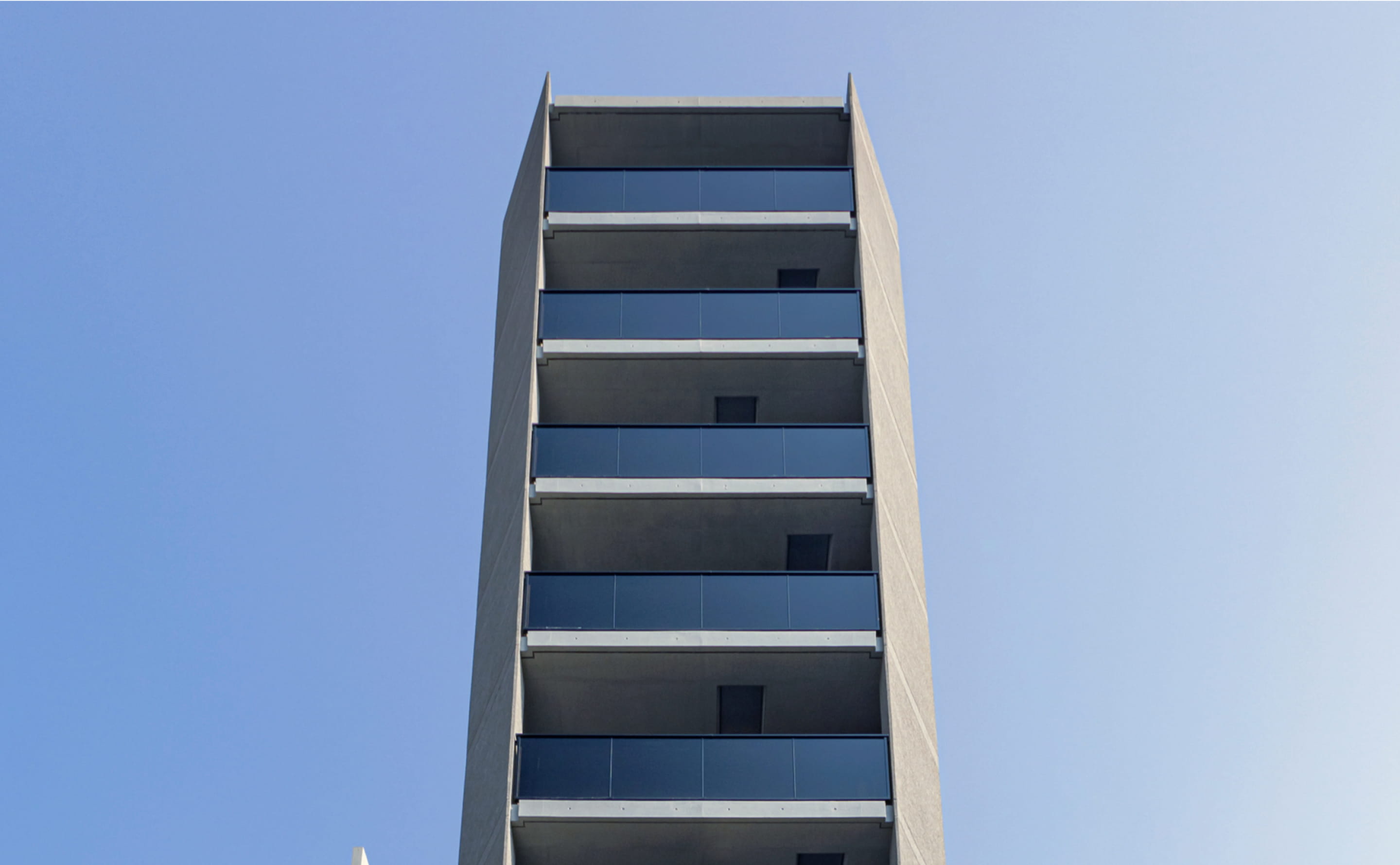 直線的なコンクリートの外観とガラス手すりが特徴のモダンな建築