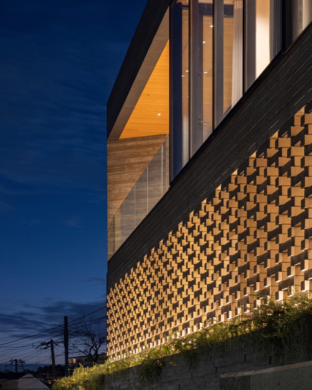 夜の空を背景に、立体的なレンガ模様の壁面がライトアップされたモダンな建築物