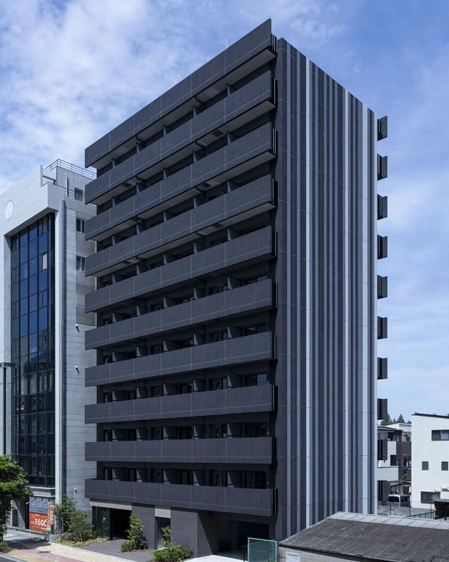 濃いグレーの外壁に水平のバルコニーラインが連なる外観を、南西側の斜めから見上げた様子